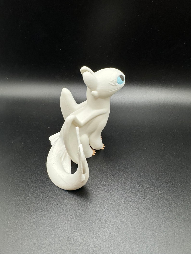May include: White dragon figurine with blue eyes and a curled tail. The dragon is standing on a black surface.