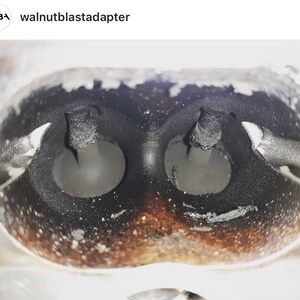 May include: Close-up of a dirty engine intake manifold with two round ports. The ports are covered in black soot and debris. The manifold is made of metal and has a rough, textured surface.