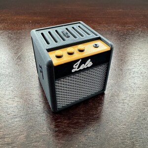 May include: A small black and gold electric guitar amplifier with the word "lele" printed on the front. The amplifier has four knobs and a speaker grill.