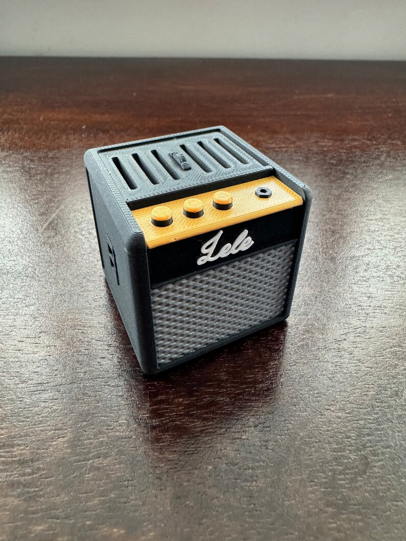 May include: A small black and gold electric guitar amplifier with the word "lele" printed on the front. The amplifier has four knobs and a speaker grill.
