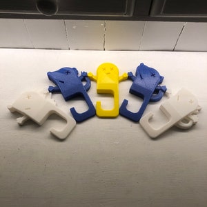 May include: Five 3D printed doorstops in the shape of a cartoon character. Two are blue, one is yellow, and two are white.