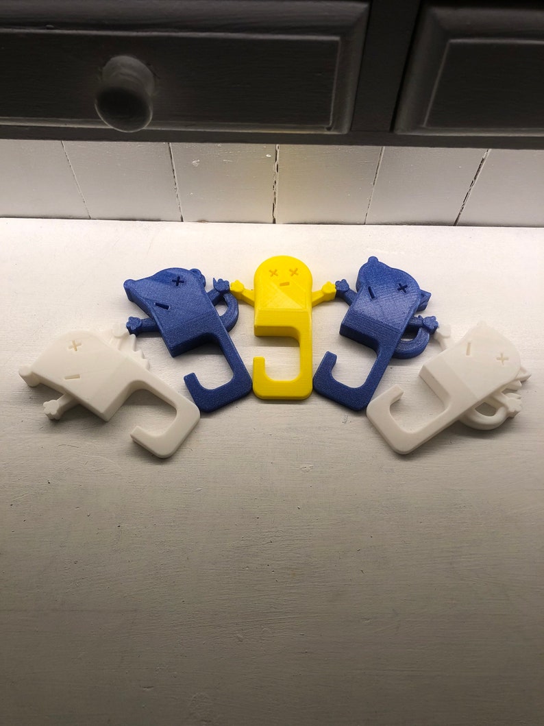 May include: Five 3D printed doorstops in the shape of a cartoon character. Two are blue, one is yellow, and two are white.