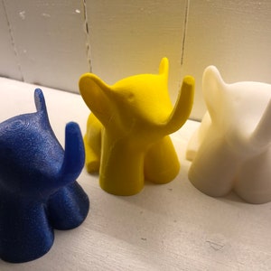 Op de afbeelding: Drie kleine olifantjes, een blauwe, een gele en een witte. De figuurtjes zijn gemaakt van plastic en hebben een gladde, glanzende afwerking.