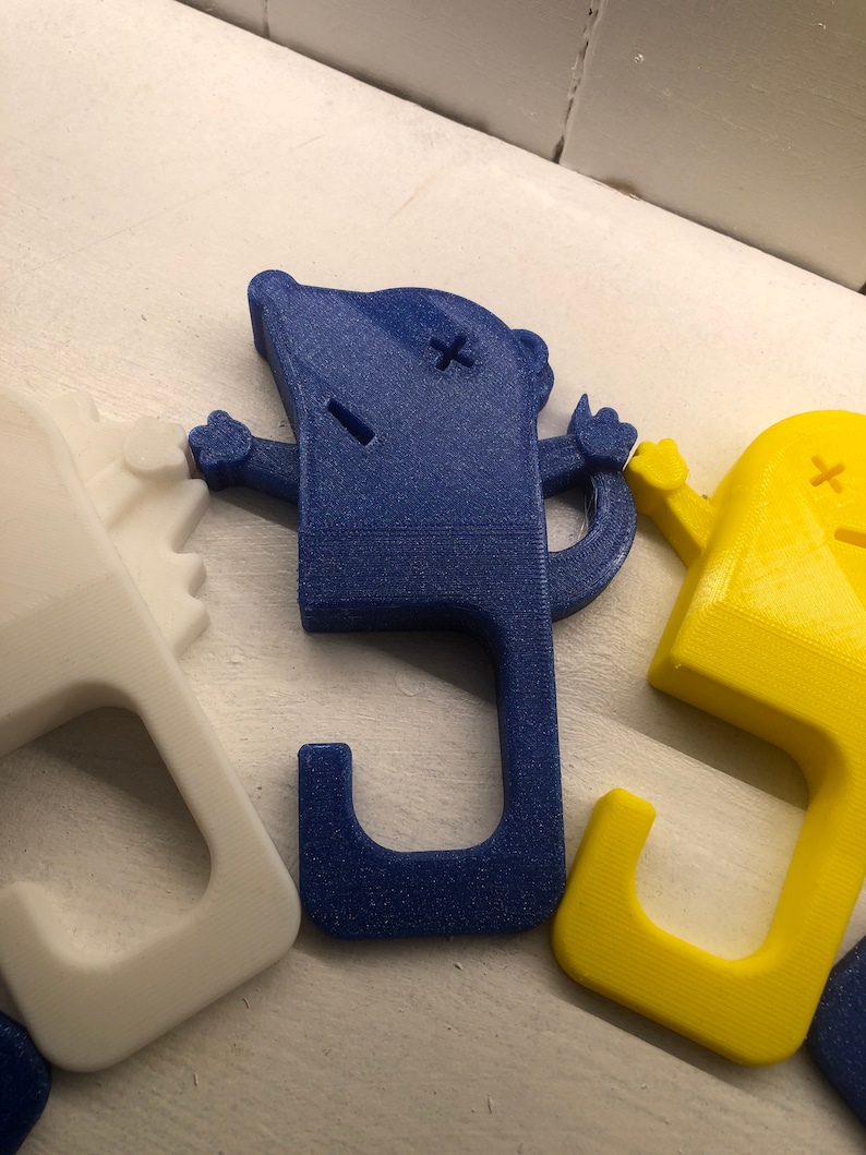 May include: Three 3D printed door handles in the shape of a cartoon character with a hook on the bottom. The handles are white, blue, and yellow.