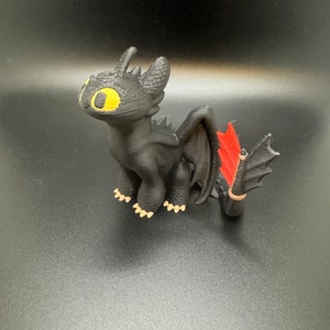 May include: A black 3D printed figurine of Toothless, the Night Fury dragon from the How to Train Your Dragon movie series. The dragon has yellow eyes, red wings, and a black tail.