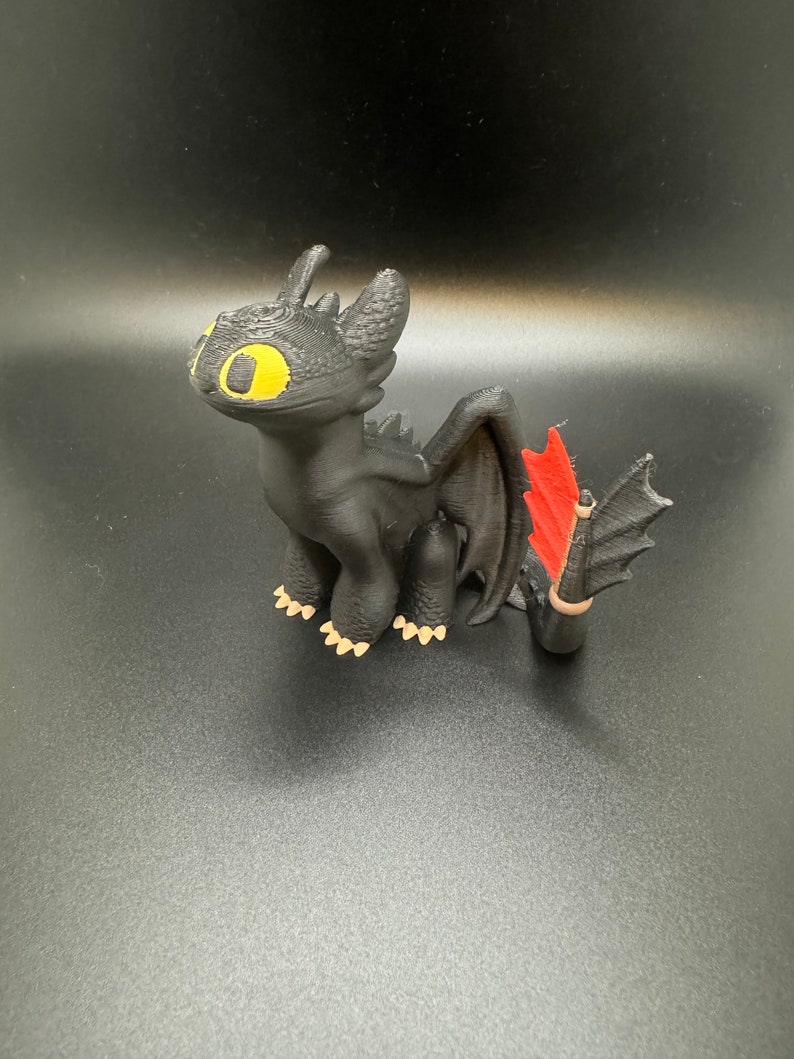 May include: A black 3D printed figurine of Toothless, the Night Fury dragon from the How to Train Your Dragon movie series. The dragon has yellow eyes, red wings, and a black tail.