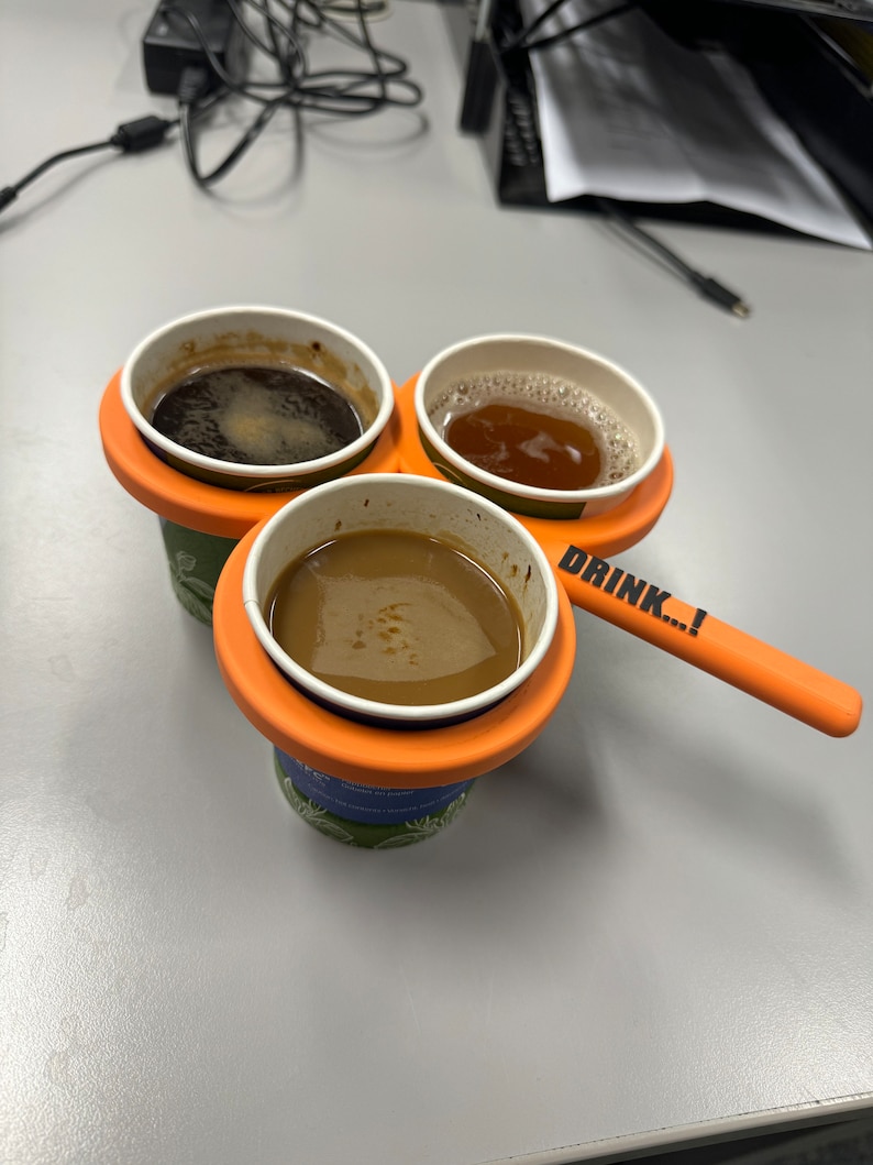 May include: Three cups of coffee in a portable orange holder with the text "DRINK...!".