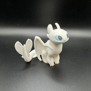 May include: White dragon figurine with blue eyes and a light pink tail. The dragon is standing on a black surface.