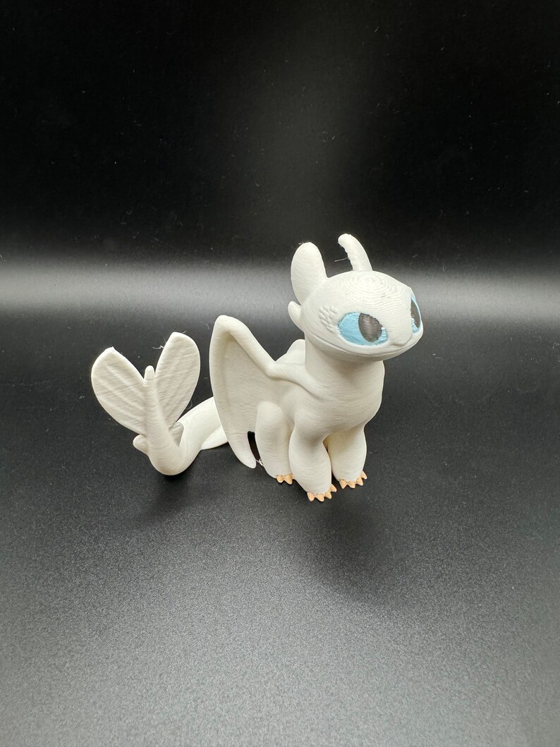 May include: White dragon figurine with blue eyes and a light pink tail. The dragon is standing on a black surface.