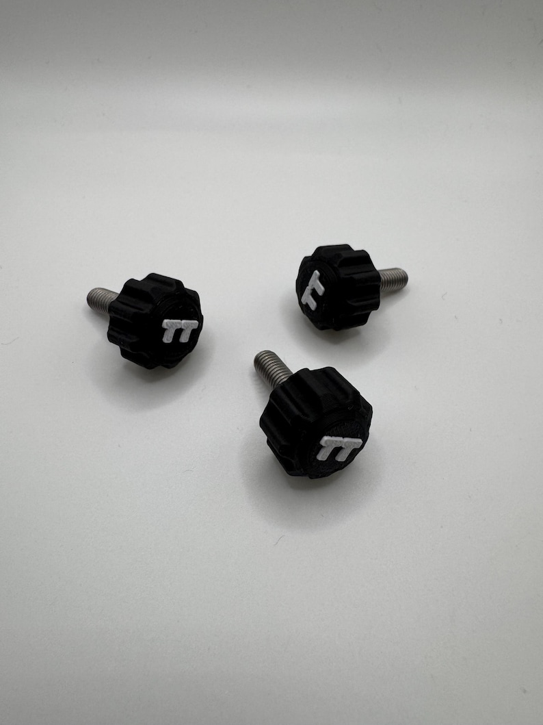 May include: Three black knobs with a silver threaded bolt. Each knob has a white "TT" logo on the top. The knobs are arranged on a white background.
