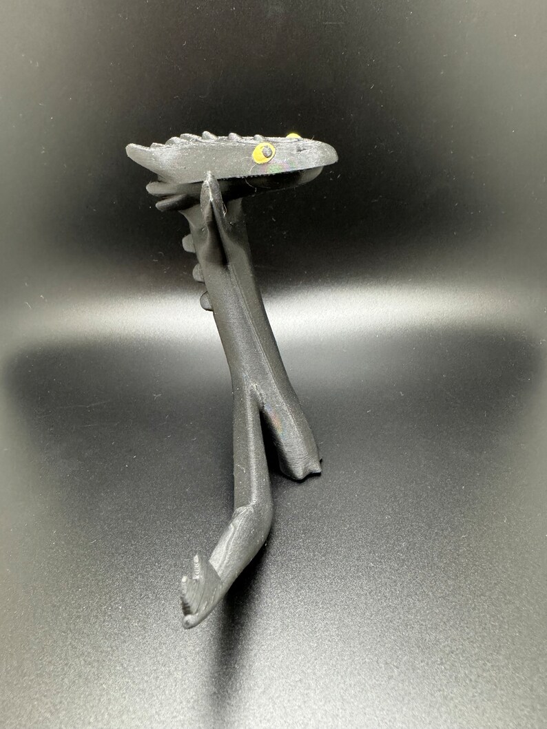 May include: Black 3D printed dragon figurine with yellow eyes. The dragon is posed in a standing position with its head tilted back and its wings spread out.