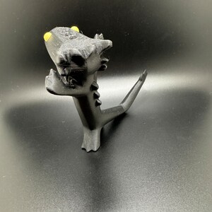 May include: A black 3D printed dragon figurine with yellow eyes. The dragon is standing on its hind legs with its tail curled up behind it.