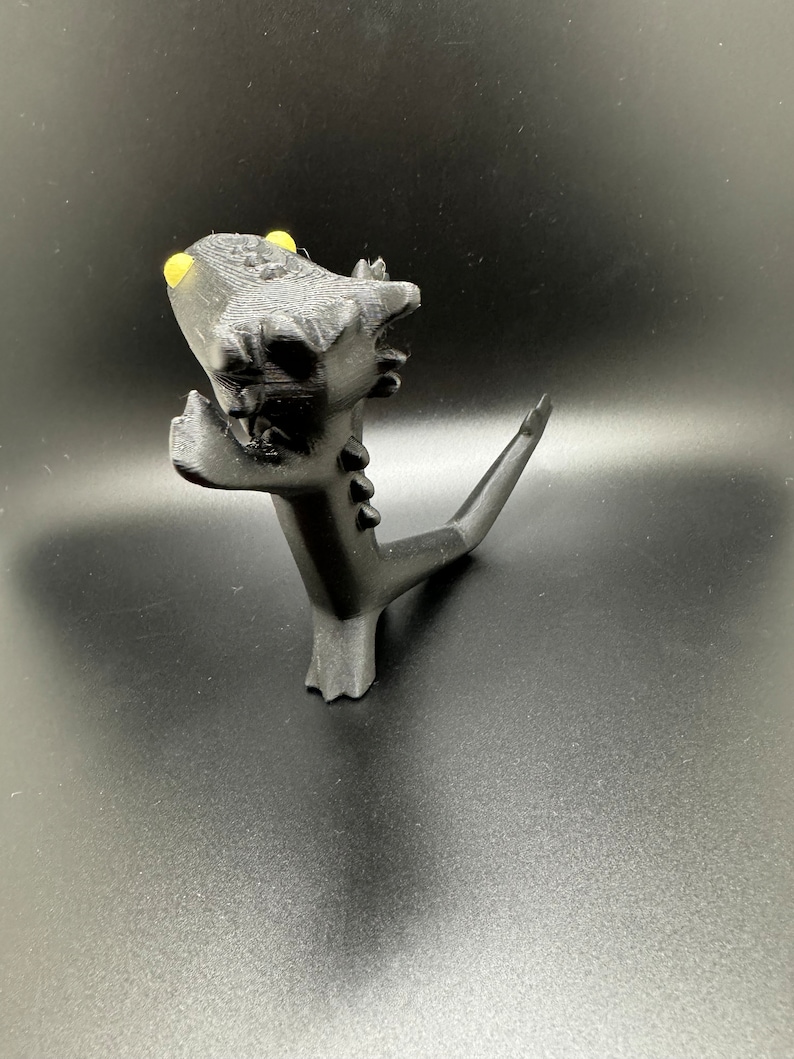 May include: A black 3D printed dragon figurine with yellow eyes. The dragon is standing on its hind legs with its tail curled up behind it.