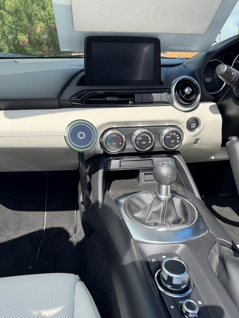 K&ouml;nnte beinhalten: Autoinnenraum mit Armaturenbrett. Es zeigt einen schwarzen Infotainment-Bildschirm, Klimaanlagen-Bedienelemente und einen manuellen Schalthebel. Ein kreisf&ouml;rmiges Ger&auml;t ist ebenfalls zu sehen.