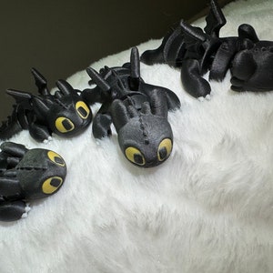 May include: Four black dragon figurines with yellow eyes, lying on a white fluffy surface.