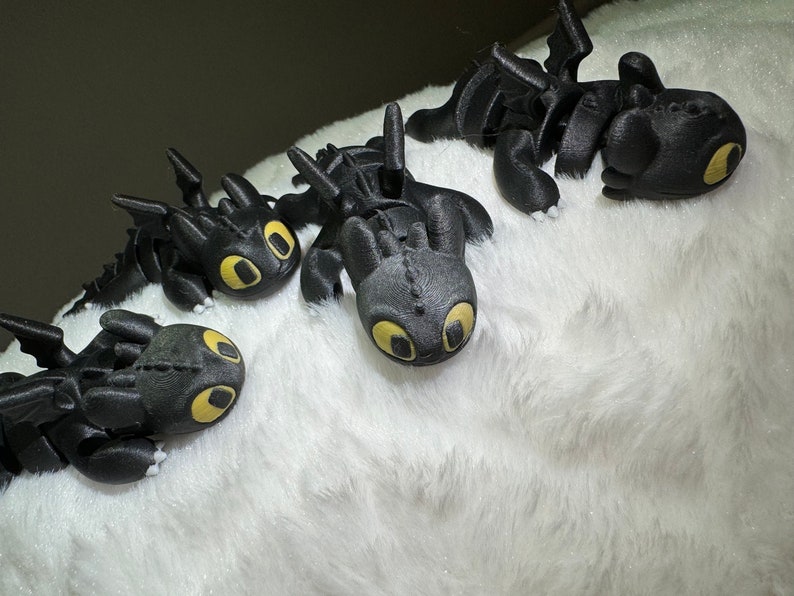 May include: Four black dragon figurines with yellow eyes, lying on a white fluffy surface.