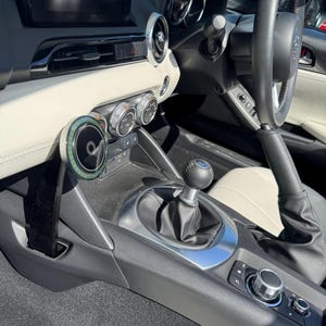 May include: Interior view of a car's dashboard, featuring a black steering wheel, a gear shift, and various control knobs. The dashboard has a black and cream color scheme, with a central console and a digital display screen.