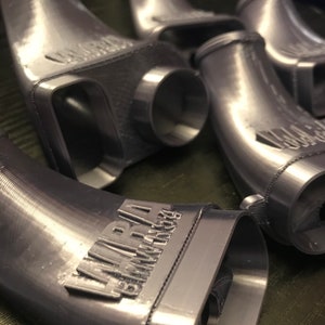 May include: Close-up of four gray 3D printed intake pipes with the text "AIRRAM PERFORMANCE" printed on one of the pipes.