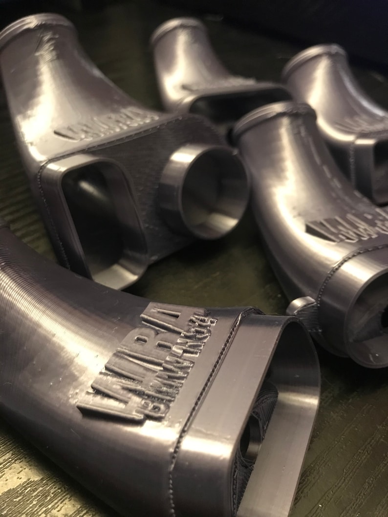 May include: Close-up of four gray 3D printed intake pipes with the text "AIRRAM PERFORMANCE" printed on one of the pipes.