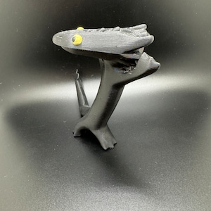 May include: A black 3D printed figurine of a creature with yellow eyes. The creature is standing on its hind legs and has its front legs raised in the air. The creature's head is tilted back and its mouth is open.