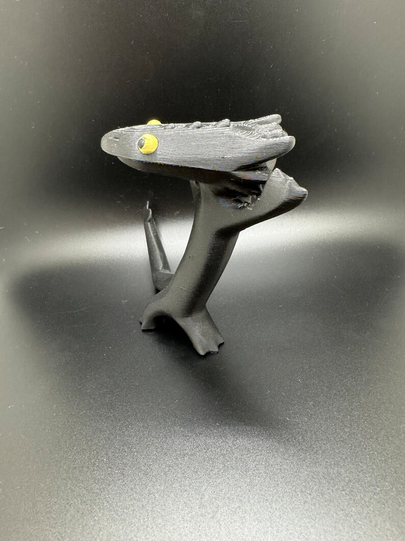 May include: A black 3D printed figurine of a creature with yellow eyes. The creature is standing on its hind legs and has its front legs raised in the air. The creature's head is tilted back and its mouth is open.