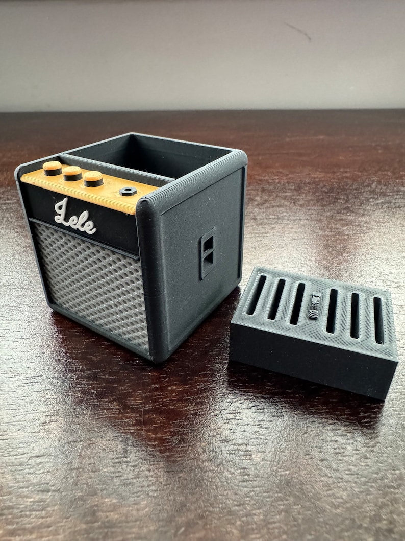 May include: Black and gray 3D printed guitar amplifier shaped desk organizer with a gold label that says "Jele" and a separate black and gray 3D printed compartment.