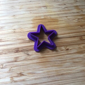 Puede incluir: Un cortador de galletas con forma de estrella de pl&aacute;stico morado sobre una superficie de madera.