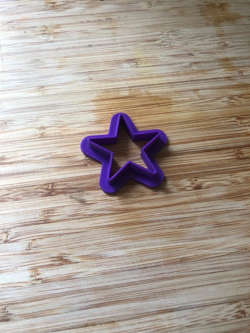Puede incluir: Un cortador de galletas con forma de estrella de pl&aacute;stico morado sobre una superficie de madera.