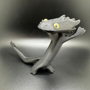 May include: A black 3D printed figurine of a dragon with yellow eyes. The dragon is standing on its hind legs with its front legs raised in the air.
