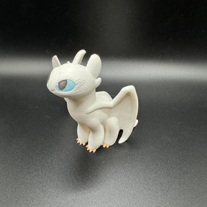 May include: White dragon figurine with blue eyes. The dragon is standing on all fours with its wings spread out behind it.
