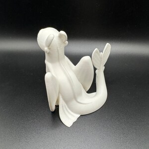 May include: White 3D printed figurine of a dragon with wings and a tail, sitting on its hind legs with its head tilted back.