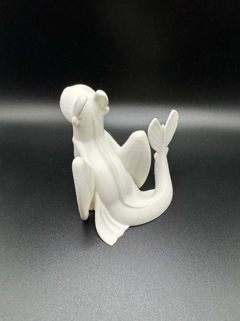 May include: White 3D printed figurine of a dragon with wings and a tail, sitting on its hind legs with its head tilted back.
