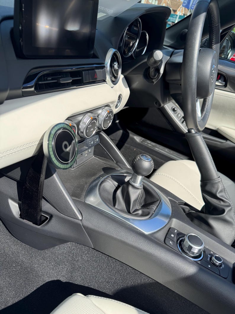 K&ouml;nnte beinhalten: Innenraum eines Autos mit Armaturenbrett, Lenkrad und Schalthebel. Das Armaturenbrett hat cremefarbene Elemente, silberne Zierleisten und einen schwarzen Infotainment-Bildschirm. Der Schalthebel ist schwarz.