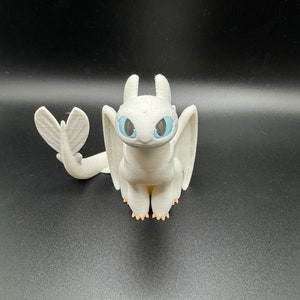 May include: White 3D printed figurine of a dragon with blue eyes. The dragon has a small tail and wings.