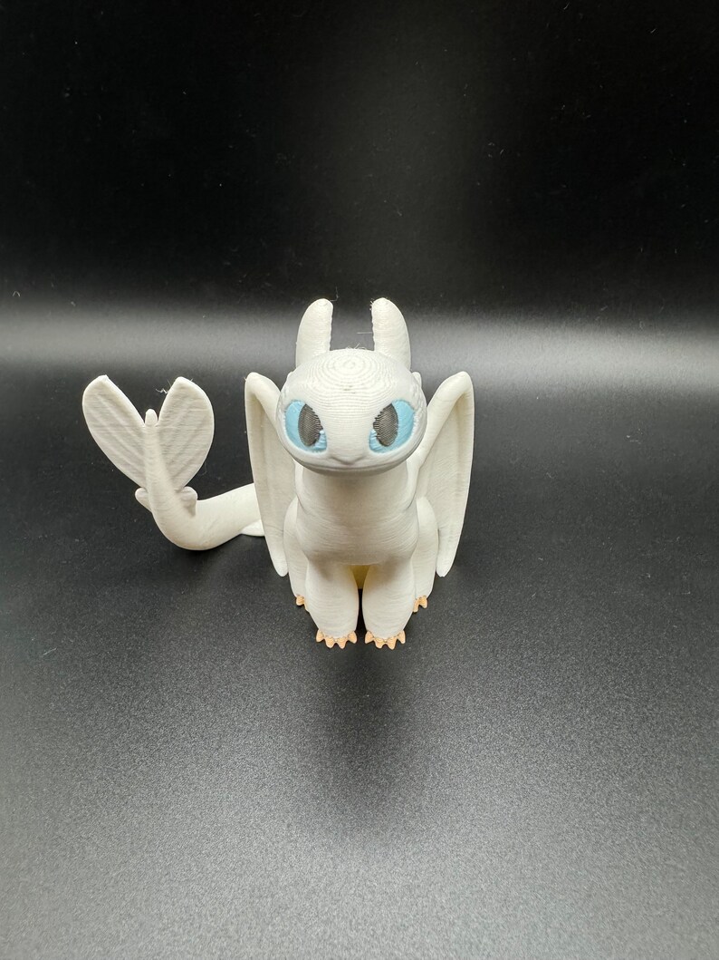 May include: White 3D printed figurine of a dragon with blue eyes. The dragon has a small tail and wings.