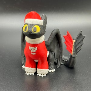 May include: A black and red 3D printed figurine of a dragon wearing a Santa hat and a red and white Christmas sweater. The dragon has a skull design on its chest.