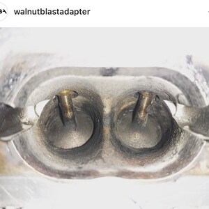 May include: Close-up of two intake ports on an engine manifold. The ports are circular and have a smooth, metallic finish. Two small, gold-colored screws are visible in the center of each port.