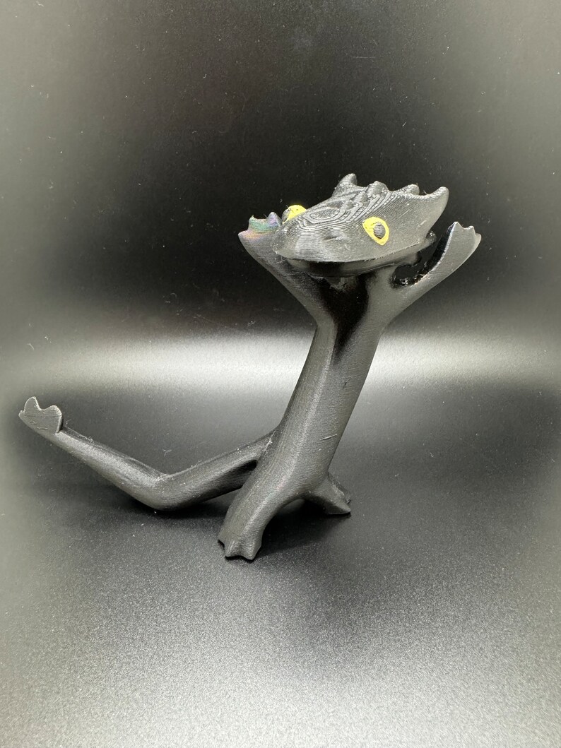 May include: A black 3D printed figurine of a dragon with yellow eyes. The dragon is standing on its hind legs with its front legs raised in the air. The dragon's tail is curled around its body.