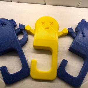 May include: Three 3D printed door handles, one yellow and two blue. The yellow handle is shaped like a ghost with a sad face and X's for eyes. The blue handles are shaped like a simple person with a single X for an eye.
