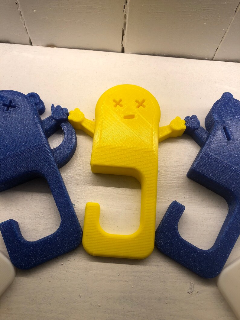 May include: Three 3D printed door handles, one yellow and two blue. The yellow handle is shaped like a ghost with a sad face and X's for eyes. The blue handles are shaped like a simple person with a single X for an eye.