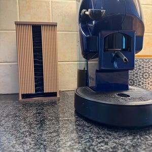 May include: A blue and black espresso machine with a coffee pod holder. The machine has a sleek design and is placed on a granite countertop. A wooden pod holder is on the left.