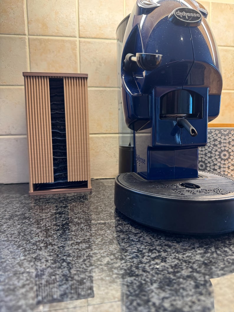 May include: A blue and black espresso machine with a coffee pod holder. The machine has a sleek design and is placed on a granite countertop. A wooden pod holder is on the left.