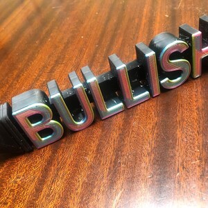 May include: A black plastic sign with the word "BULLISH" in rainbow iridescent letters.