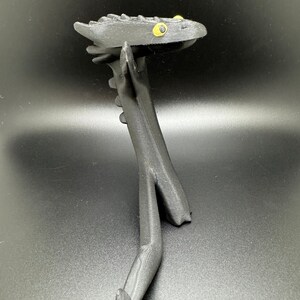 May include: Black 3D printed dragon figurine with yellow eyes. The dragon is standing on its hind legs with its front legs outstretched.