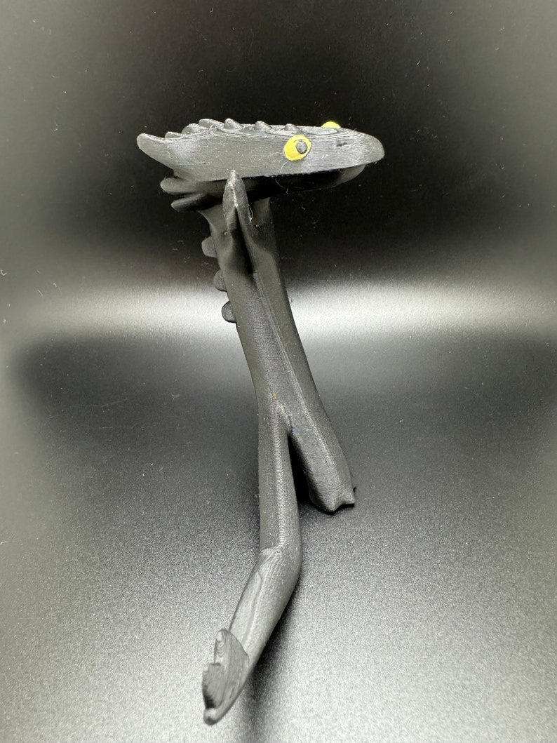 May include: Black 3D printed dragon figurine with yellow eyes. The dragon is standing on its hind legs with its front legs outstretched.