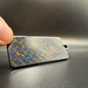 May include: A black rectangular tag with a holographic iridescent pattern. The tag has a small hole at the top for attaching a string or ribbon.