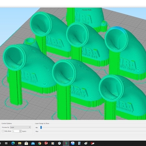 May include: A 3D printed model of a green plastic elbow pipe fitting. The fitting has a round opening on one end and a rectangular opening on the other end. The fitting is labeled "MARA" on the side.