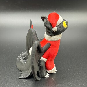 May include: A black 3D printed figurine of a dragon wearing a red and white Santa Claus suit and hat.