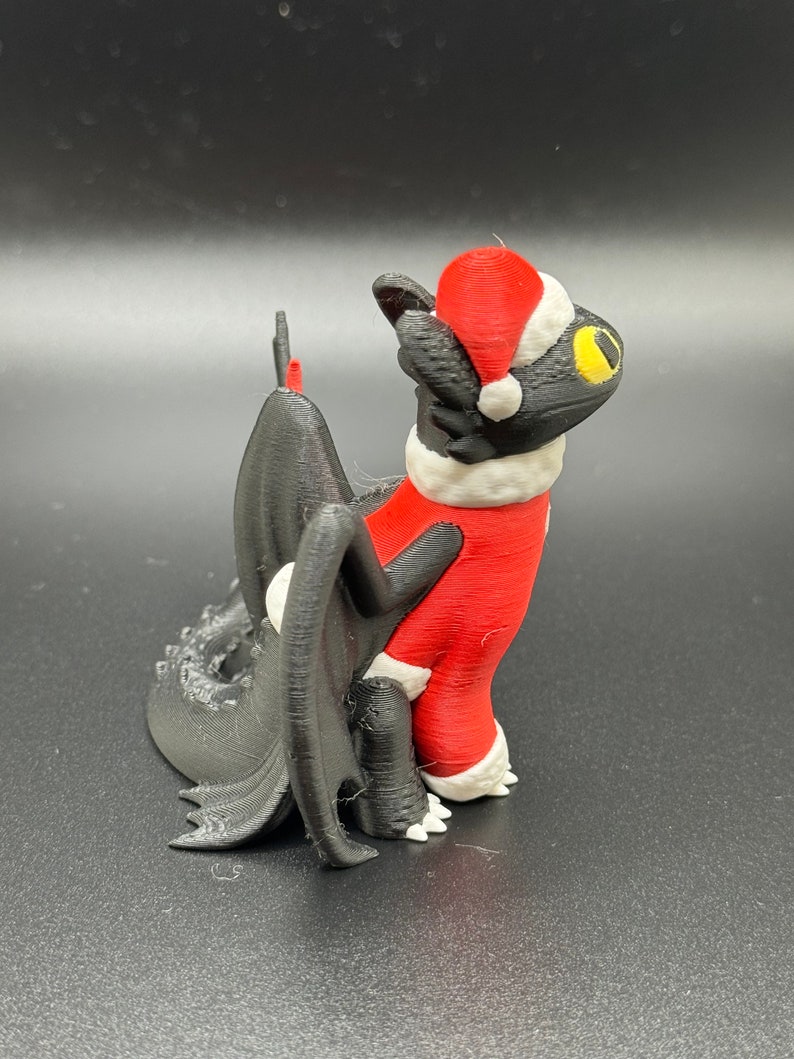 May include: A black 3D printed figurine of a dragon wearing a red and white Santa Claus suit and hat.