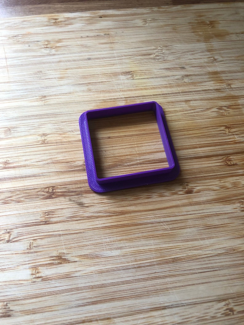 Puede incluir: Un cortador de galletas cuadrado de pl&aacute;stico morado.